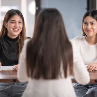 Two interviewers smile and take notes while speaking with a candidate seated across from them at a table.