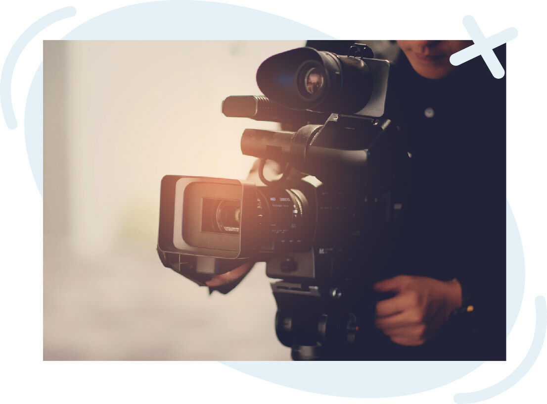Close-up of a professional video camera being operated by a person, with warm light flaring on the lens.