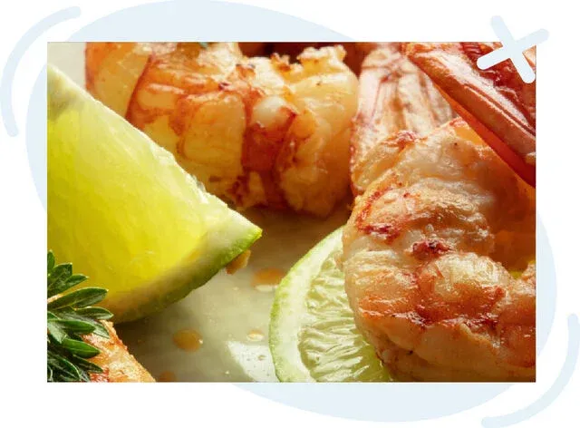 Close-up of grilled shrimp with lime wedges and herbs on a plate.