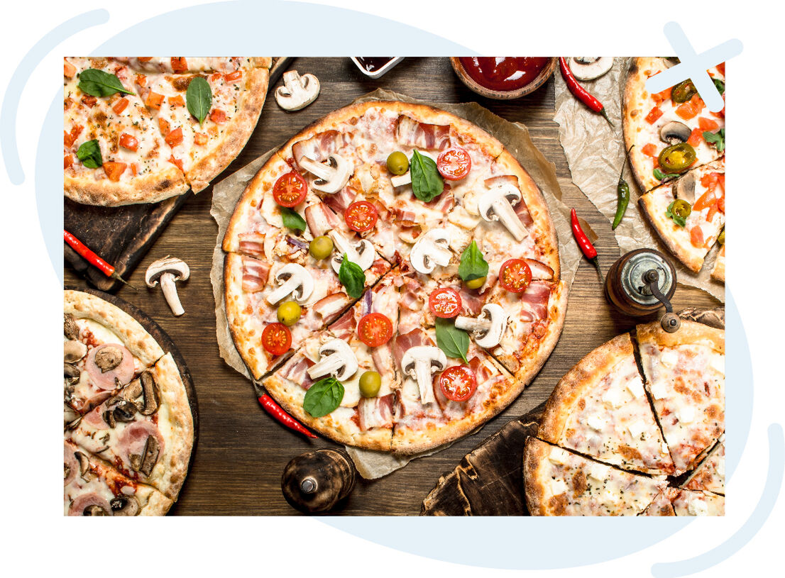 Assorted pizzas on a rustic wooden table, with a central pizza topped with mushrooms, cherry tomatoes, bacon, olives, and basil leaves.