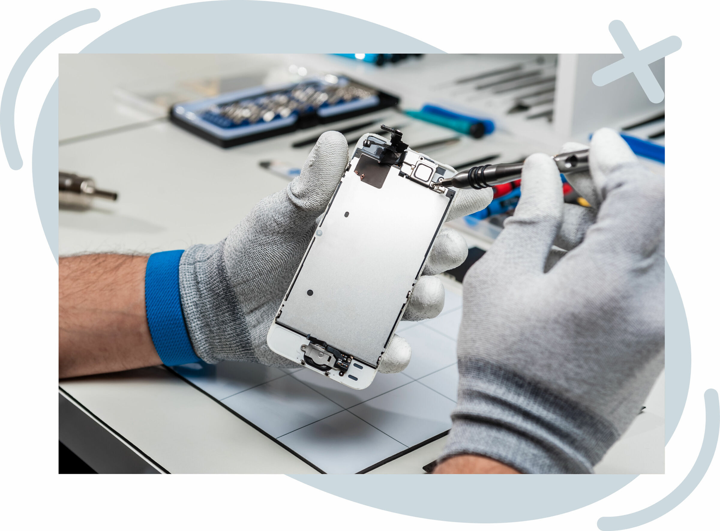 Technician wearing gray gloves repairing a smartphone screen assembly with a precision screwdriver at a clean workbench.