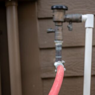 Close-up of a red garden hose connected to an outdoor plumbing valve against a brown wooden wall.