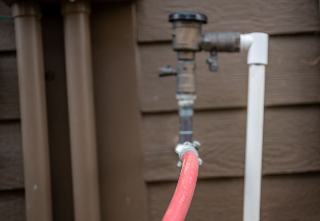 Close-up of a red garden hose connected to an outdoor plumbing valve against a brown wooden wall.