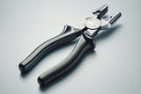 Close-up of a pair of metal pliers with black textured handles placed on a smooth light gray surface.