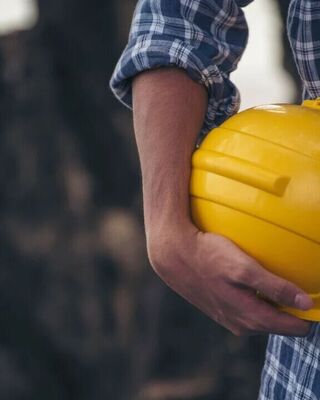 Close-up of a person in a plaid shirt holding a yellow hard hat at their side.