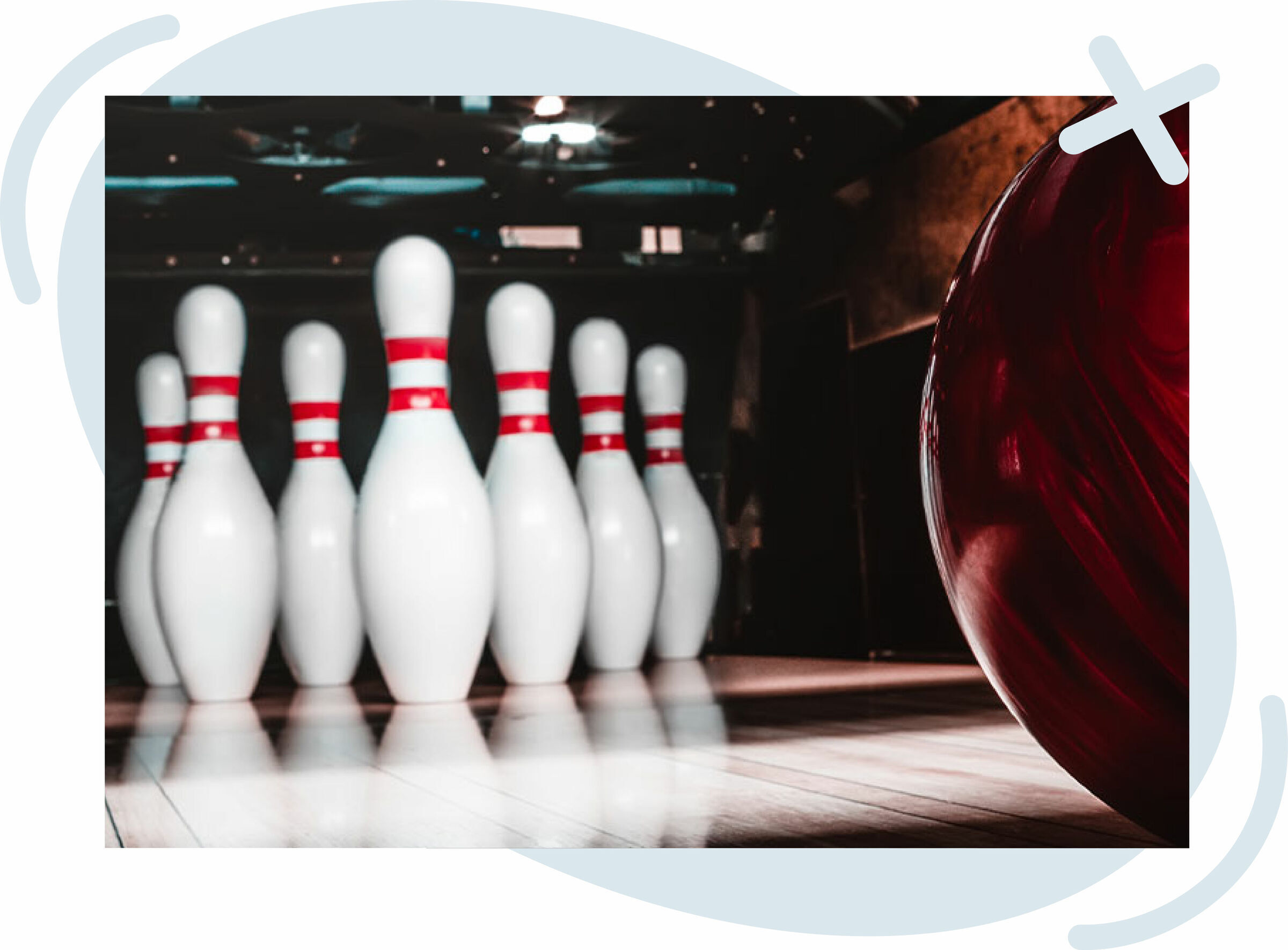 Close-up of a bowling lane with a red bowling ball approaching a set of white pins with red stripes.