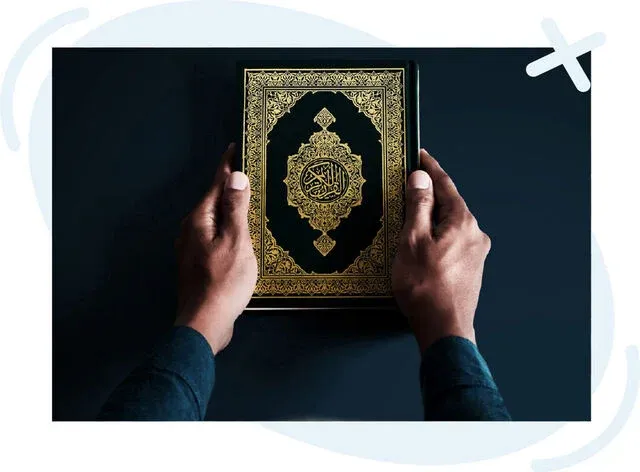Hands holding an ornate book with gold Arabic calligraphy on a dark background.