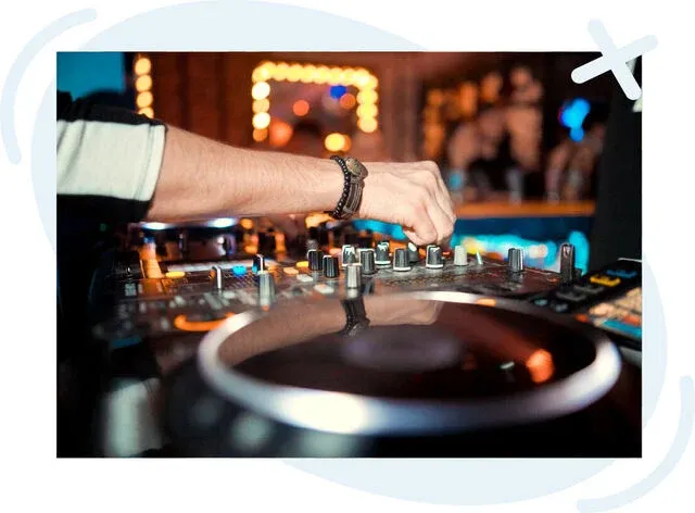 Close-up of a DJ’s hand adjusting knobs on a mixer in a dimly lit club.