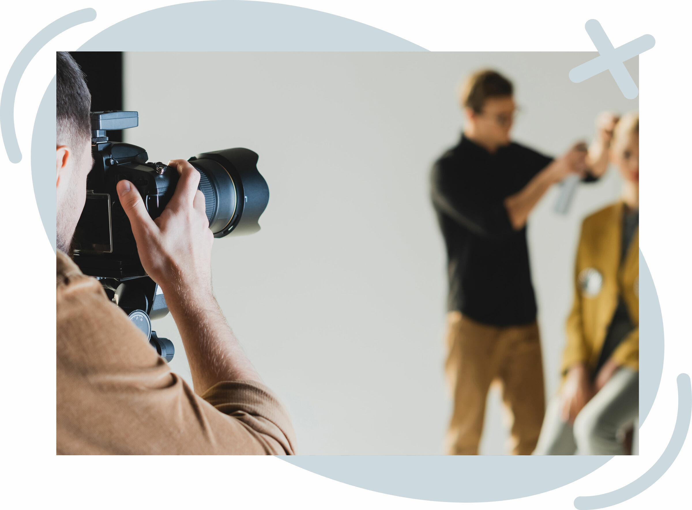 Photographer taking a shot in a studio while a stylist works on a subject in the background.