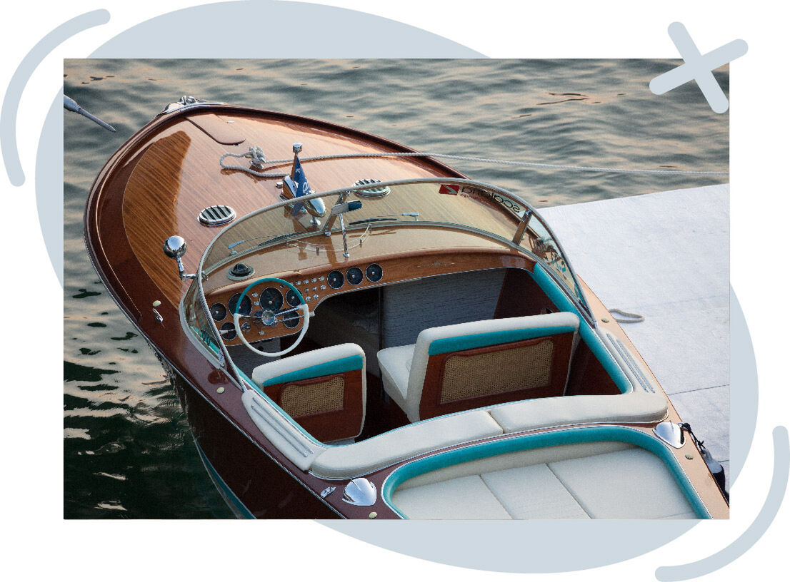 Top-down view of a classic wooden speedboat moored beside a dock, featuring cream and turquoise upholstery and a curved windshield on calm water.