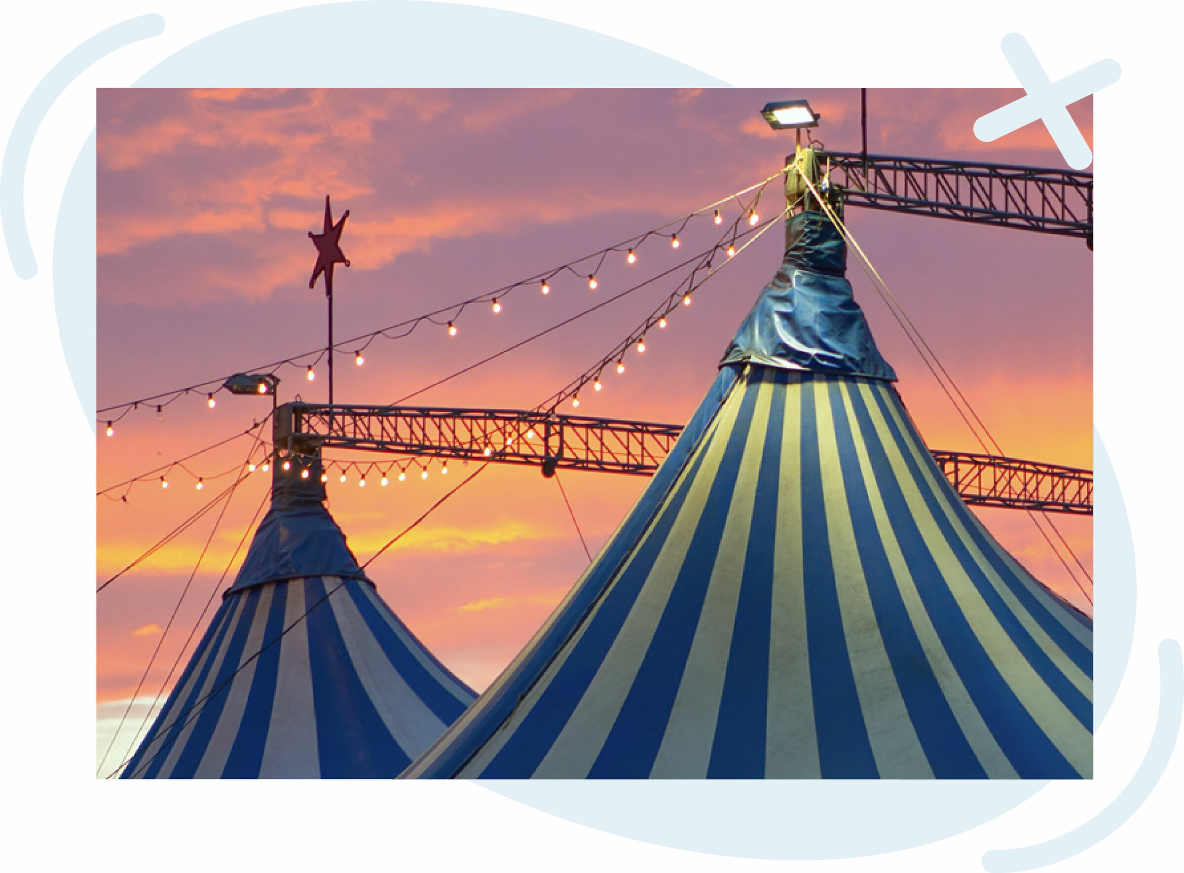 Blue-and-white striped circus tents at dusk with string lights and a vivid orange-pink sky.