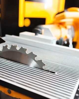 Close-up of a table saw with a circular blade protruding through a ribbed metal surface in a workshop.