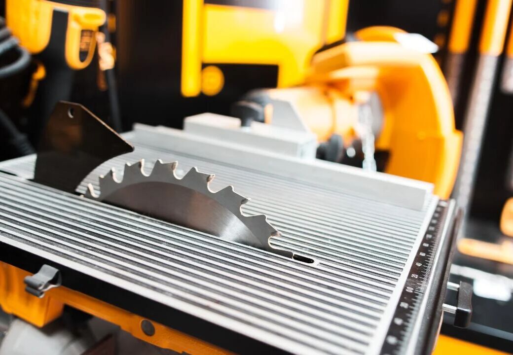 Close-up of a table saw with a circular blade protruding through a ribbed metal surface in a workshop.