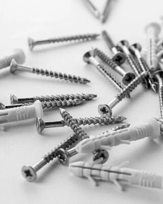 Close-up of scattered metal screws and white plastic wall anchors on a plain surface.