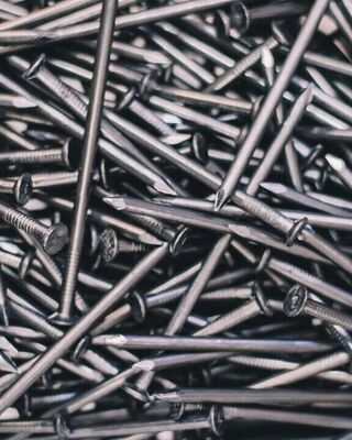 Close-up view of a scattered pile of shiny metal nails with pointed tips and flat textured heads, overlapping in various directions.